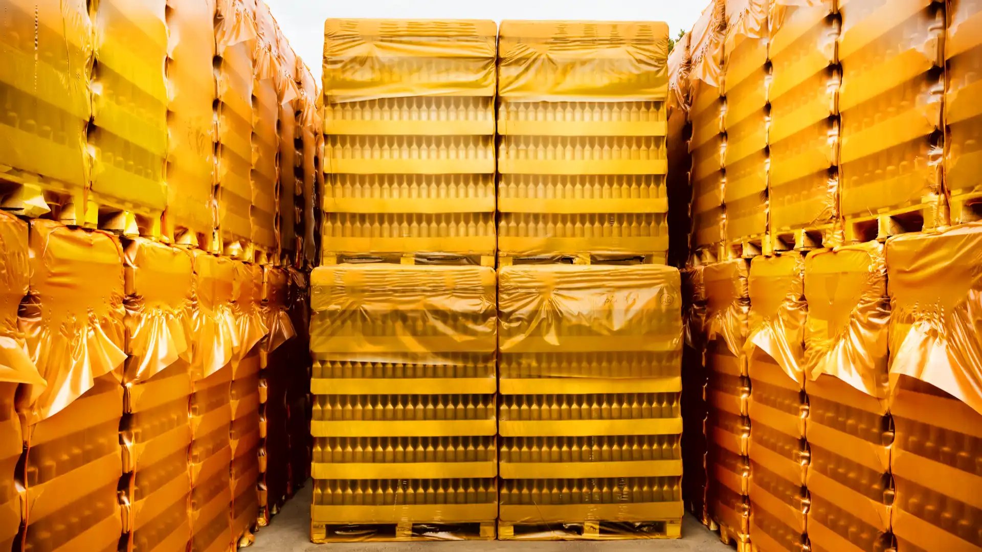 palletized-goods Stacked yellow-wrapped pallets stored in a tightly packed aisle