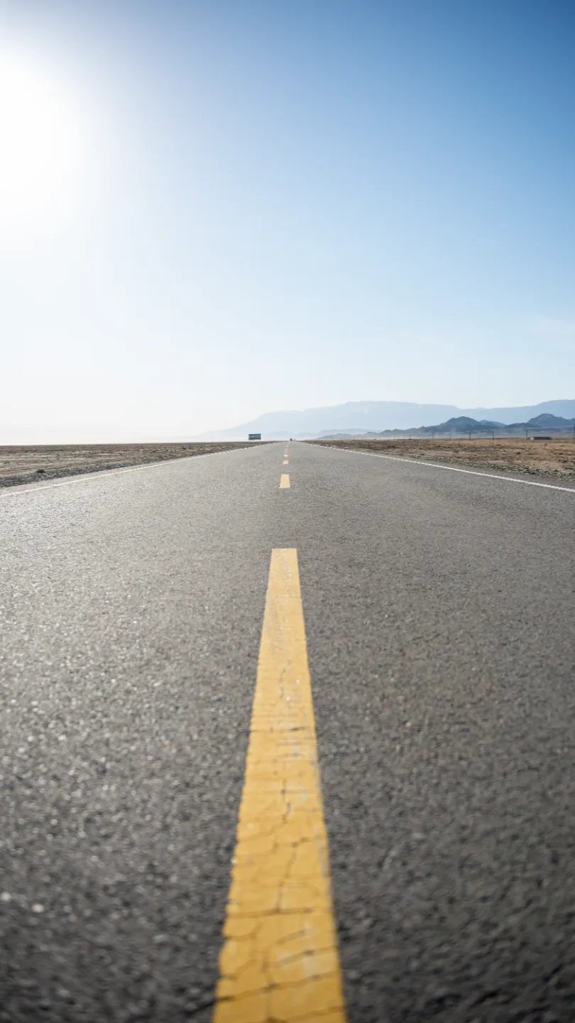 Empty two-lane highway with yellow centreline stretching toward distant mountains