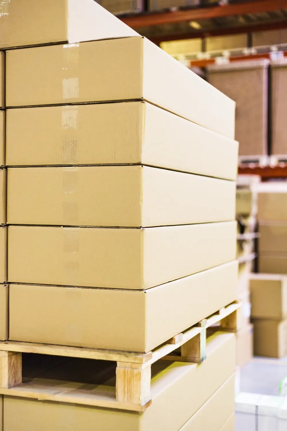 Flat cardboard cartons stacked high on a wooden pallet inside a warehouse