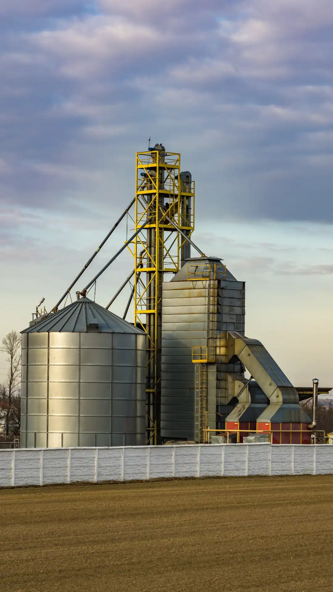 Steel grain silos and elevator complex beside a farm field, a common Super B grain-hauling pickup point