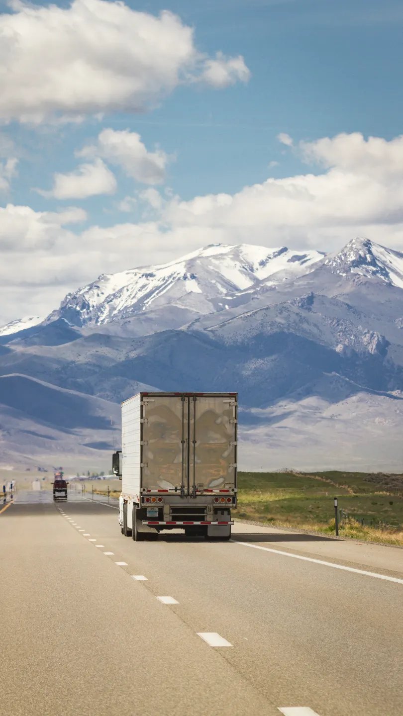 Semi truck driving toward snowcapped mountains on open highway