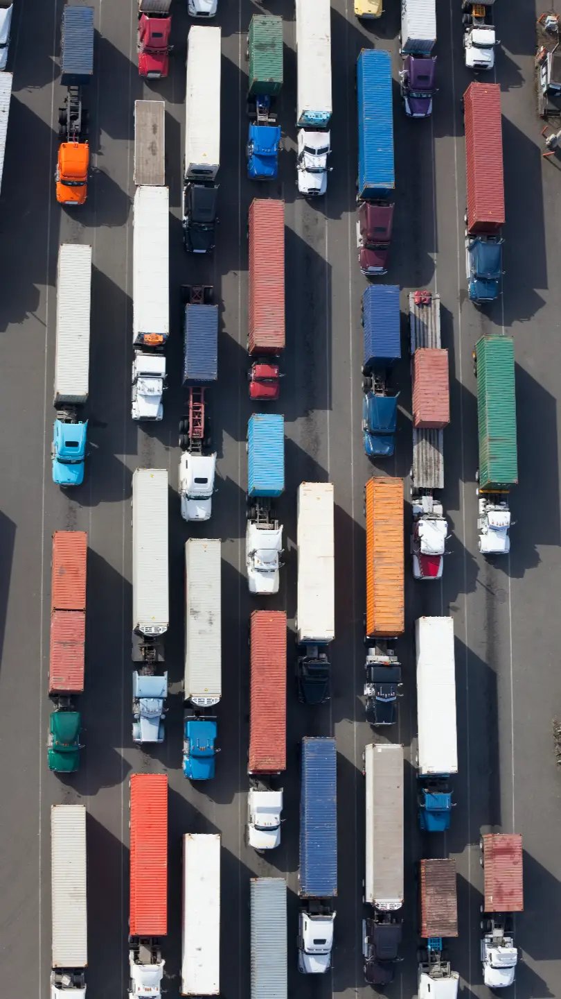 Top-down aerial of semi trucks with colourful trailers and containers queued in a freight yard