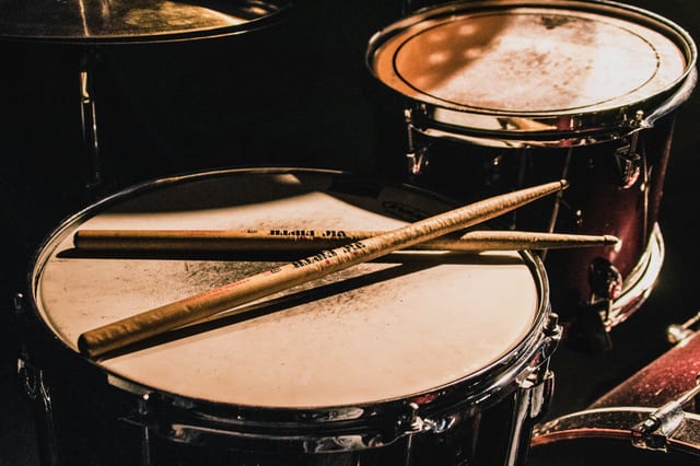 close up of a drum set with two wooden drumsticks resting on the drumhead moody lighting in the background drummer hearing drummers and hearing loss protecting your ears the audiology place