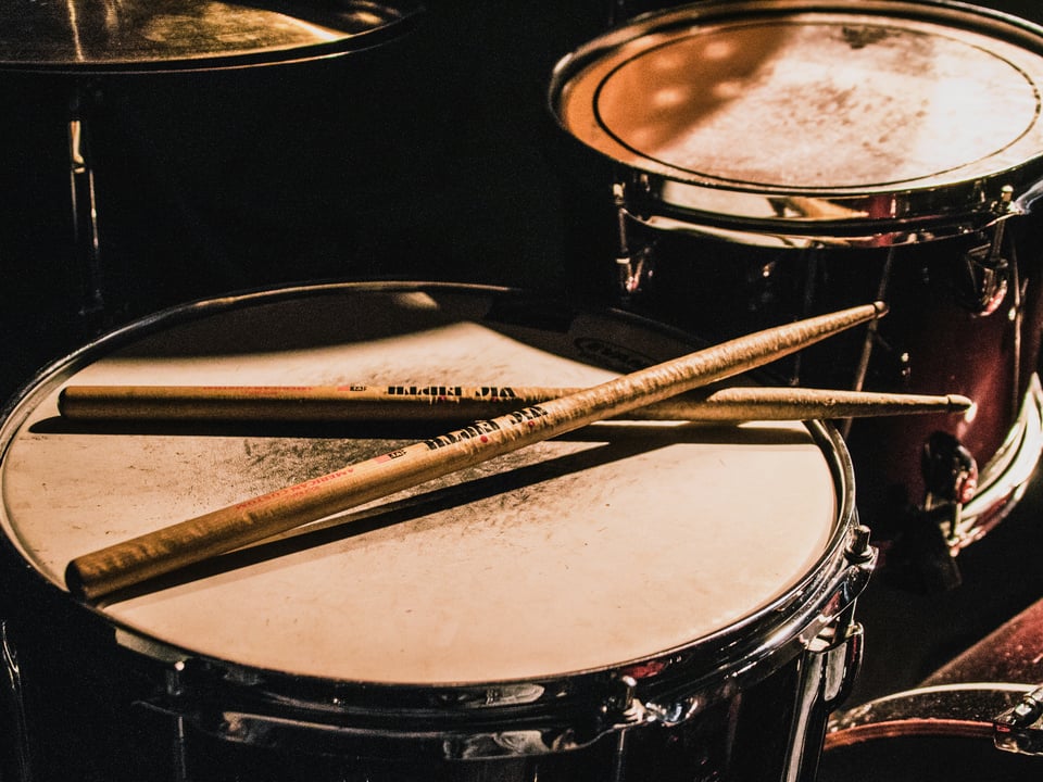 close up of a drum set with two wooden drumsticks resting on the drumhead moody lighting in the background drummer hearing learn the audiology place