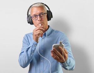 Home-Page-300x233 - The Audiology Place older man wearing headphones holds a smartphone finger to lips in a thinking pose home page 300x233 the audiology place sydney independent hearing clinic