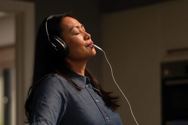 woman wearing over ear headphones singing into a headset mic in a recording studio relaxing lenire moments 768x512 lenire tinnitus treatment the audiology place