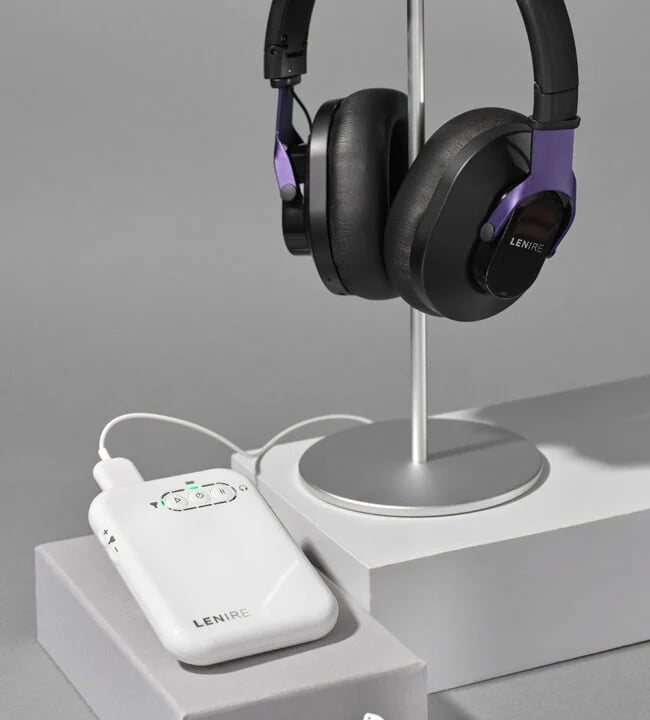 Black over-ear headphones with purple accents resting on a metal stand, connected to a white LENIRE control module on a gray surface.