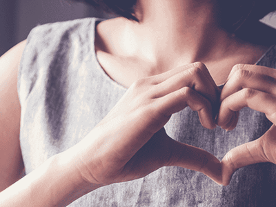 Heart-shaped hands at woman's chest, symbolizing community and kindness, supporting Timebank Ireland initiatives and volunteering efforts.