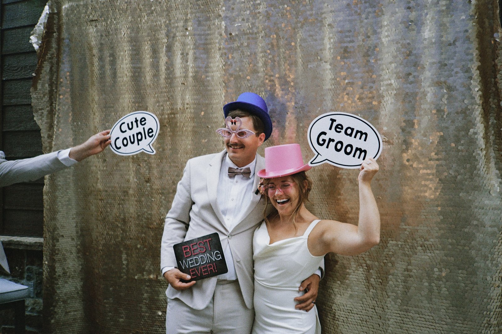 A couple with props at Firefly's gold-sequin open-air photo booth at a Glenwood Canyon wedding — Photo: Kelly Miller Studios