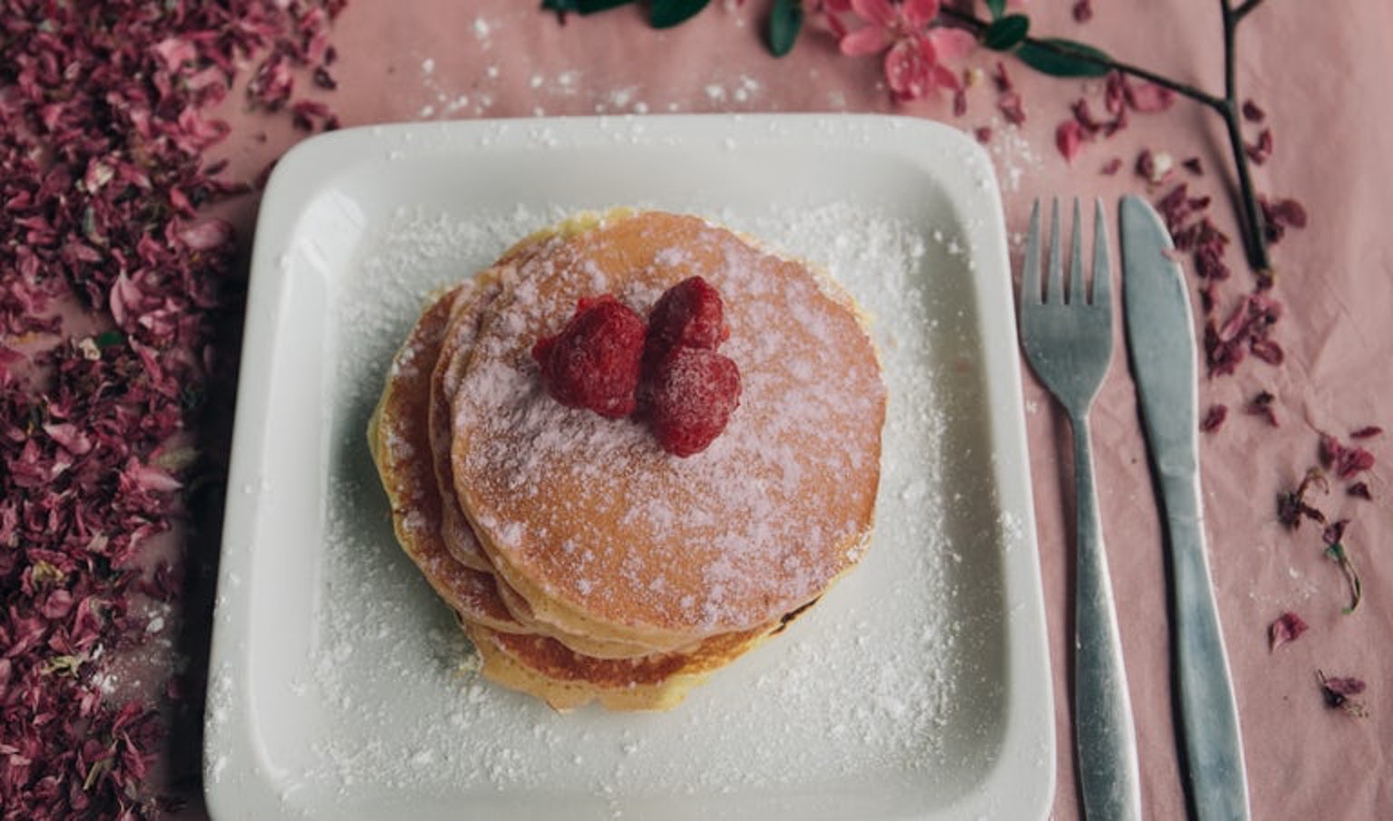 247 Easy Marijuana Edibles Recipes to Make at Home 12 pancakes on a plate with raspberries on top, the plate is on a pink tablecloth
