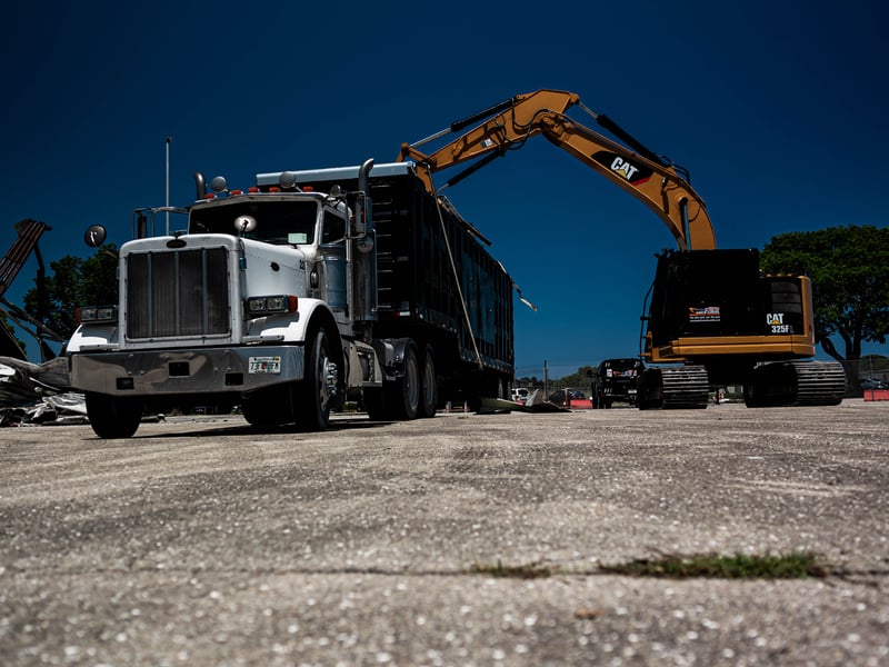 Dump truck and excavator hauling demolition debris from airport hangar site in Boca Raton, 2026