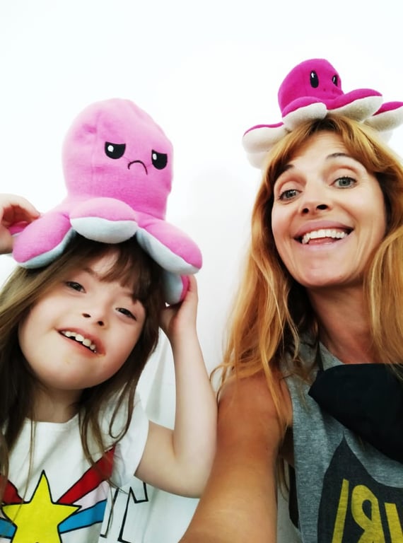 una niña con síndrome de Down un pulpo rosa en la cabeza y una señora que es su mamá con un pulpo rojo en la cabeza