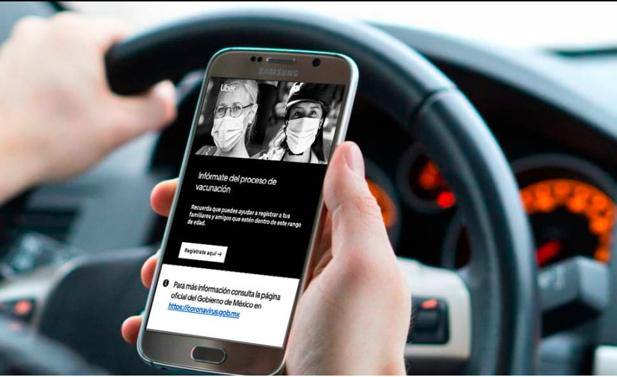 Fotografía de las manos de una persona sosteniendo un teléfono celular mientras está dentro de su automóvil sosteniendo el volante, en la pantalla del teléfono aparece una imagen de la plataforma de Uber con dos fotografías de mujeres a blanco y negro, sus rasgos no se alcanzan a distinguir.