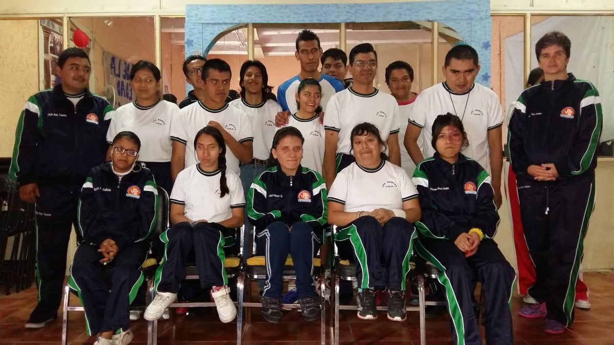 Fotografía de mejores épocas. Un nutrido grupo de jóvenes, hombres y mujeres, con diferentes discapacidades se colocan en diferentes filas para armar un grupo. Hasta adelante están colocadas las personas usuarias de sillas de ruedas, y en la parte posterior hay un par de filas donde las personas están de pie. El grupo ofrece la imagen de un equipo deportivo y visten el uniforme de pants de la unidad Las Garzas.