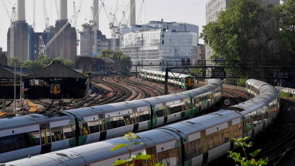 Fotografía de dos trenes de cercanías en Londres. Los vagones no se aprecian en detalle, pero fueron captados en una curva, lo que permite abrir la toma y ver en la parte trasera imágenes de una zona industrial.