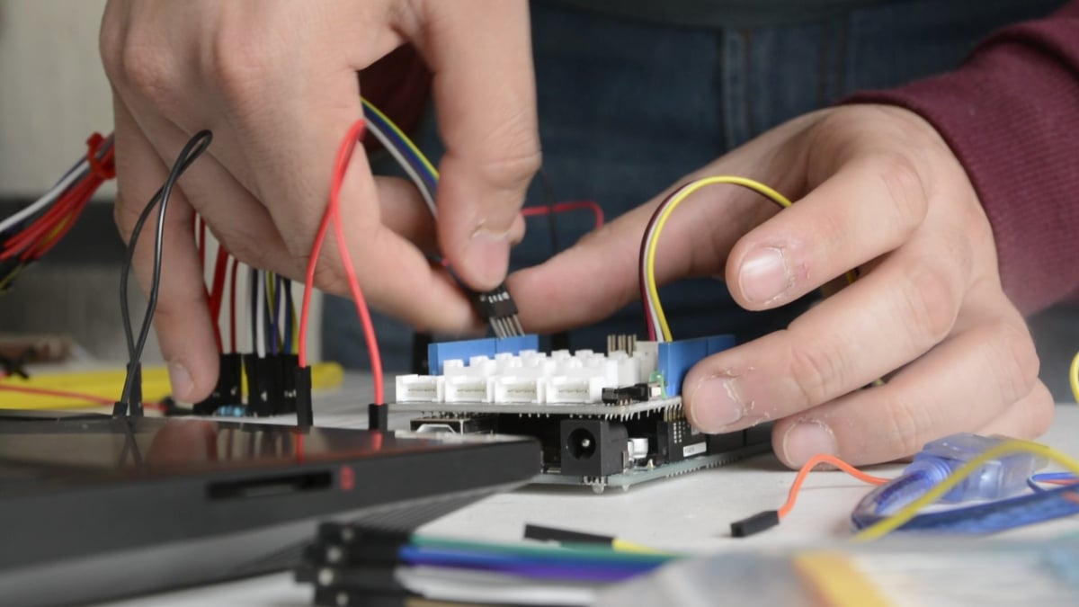 Prototipo del dispositivo de asistencia que traduce textos en Sistema Braille a audio diseñado por estudiantes del Tec de Monterrey. En la fotografía se ven unas manos, ante una especie de teclado blanco, más pequeño que una de las manos, al que están conectados unos cables.