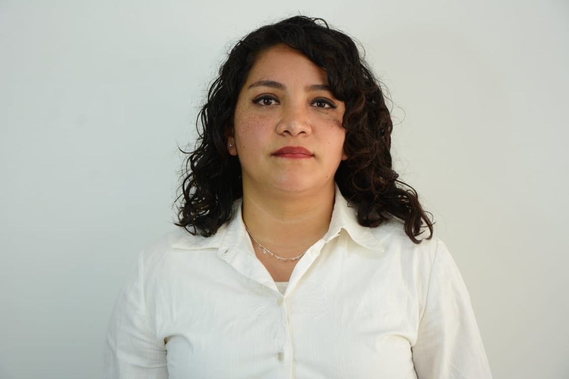 Fotografía de Norma Narváez Aguilar, una mujer joven de tez latina, cabello negro, un poco ondulado, suelto, aparece con una ligera sonrisa frente a la cámara, lleva puesta una blusa de color blanca con manga larga, el fondo de la imagen es color blanco.
