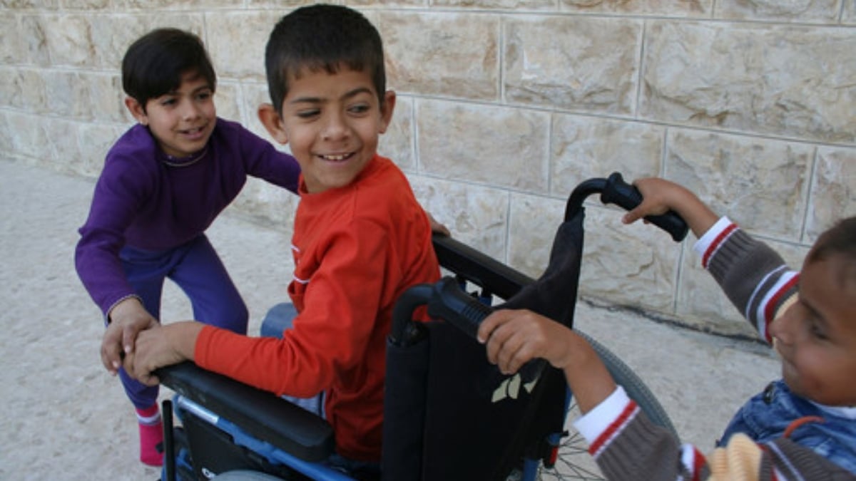 Tres niños jugando, uno de ellos es usuario de silla de ruedas