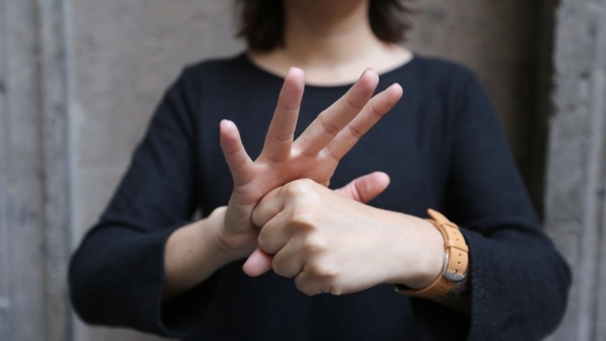 Fotografía de una intérprete de Lengua de Señas Mexicana que indica cómo hacer la seña para coronavirus: con un mano se hace un puño y la otra se coloca arriba con los dedos abiertos para formar una corona.