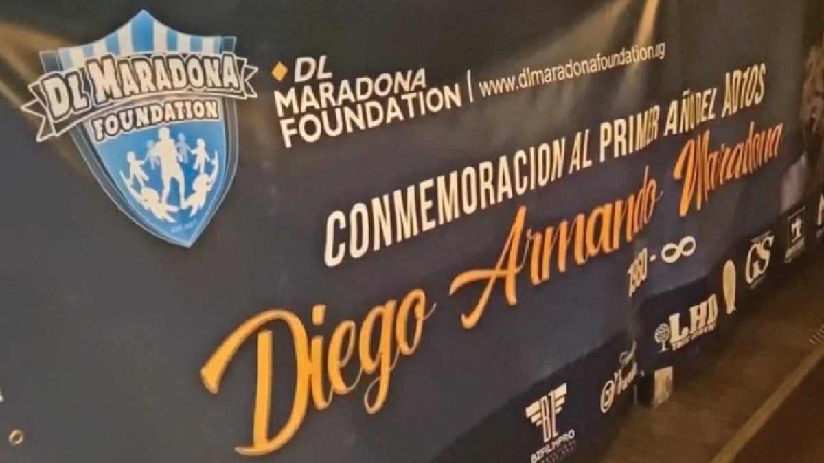 Fotografía de un banderían en fondo negro que en letras blancas dice DL Maradona Foundation, conmemoración al primer año del adiós Diego Armando Maradona 1960 símbolo de infinito. Y al pie hay varios logotipos, además del escudo de la fundación en el extremo superior.