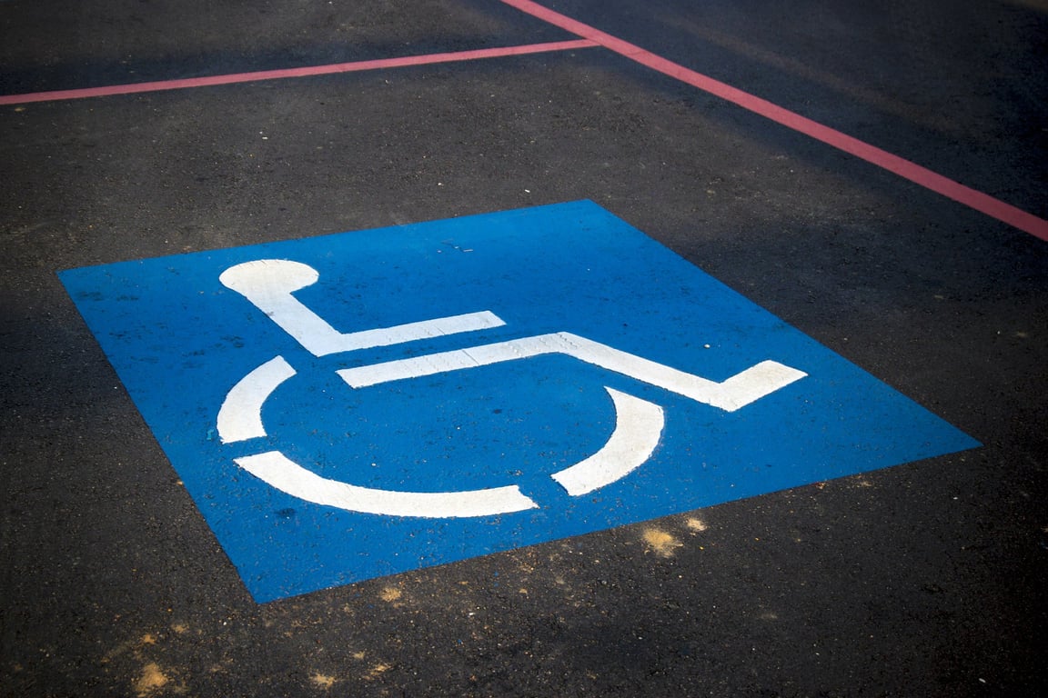 Fotografía del piso de color gris de un estacionamiento público que tiene un estampado de color azul en el fondo con una silueta de una persona usuaria de silla de ruedas de color blanco.