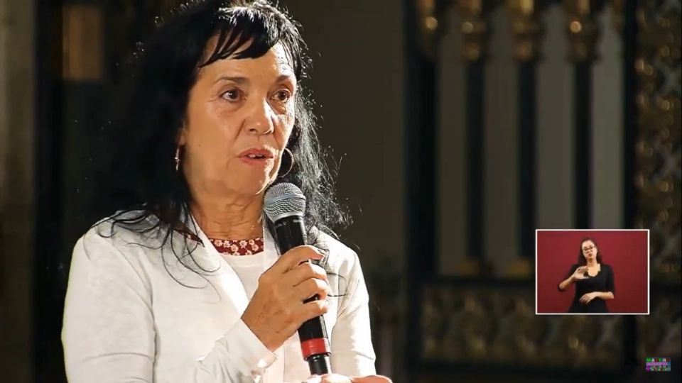 Captura de pantalla de la conferencia matutina del presidente en donde aparece Nuria Fernández, una mujer de edad adulta, cabello quebrado con algunas canas, toma un micrófono con la mano izquierda, lleva puesto un saco de color blanco.