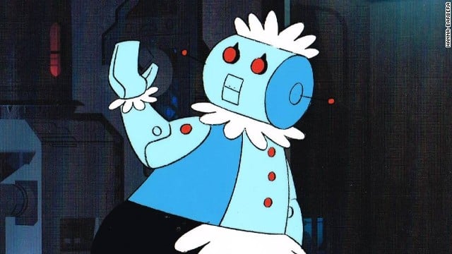 Captura de pantalla del programa “Supersónicos” en donde aparece Robotina, un personaje animado de una robot auxiliar en las tareas del hogar, su cuerpo está hecho de metal, tiene puesto un uniforme de mantel blanco con falda negra, en lugar de pies tiene ruedas, sus manos tienen forma de pinzas, saluda hacia la derecha.