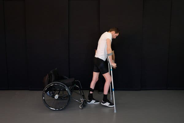 Fotografía de un hombre con discapacidad motriz que camina con el apoyo de dos muletas dejando detrás su silla de ruedas.