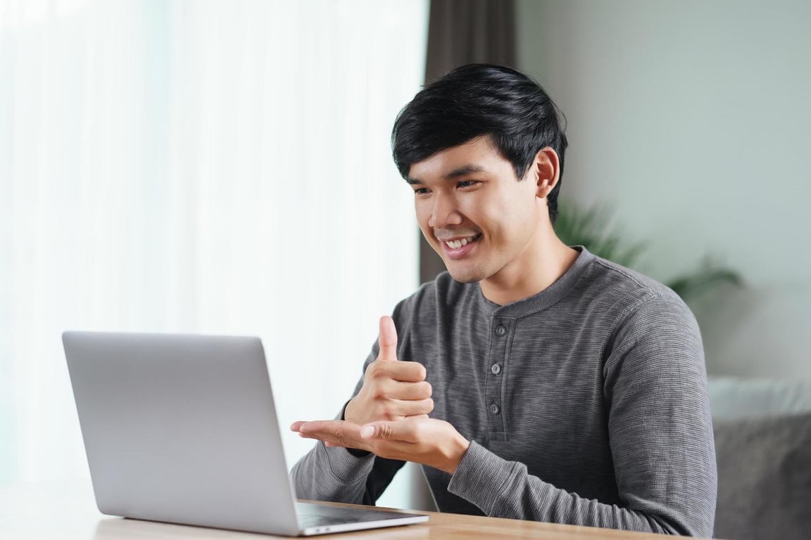 Fotografía de un joven sordo gesticulando una seña frente a una laptop.