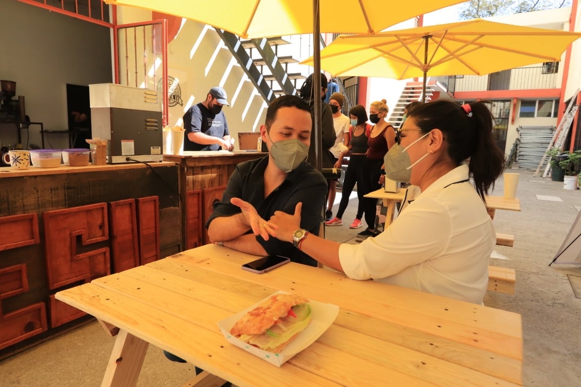 Cafetería resiliente con comensales y meseros comunicándose en Lengua de Señas Mexicana.