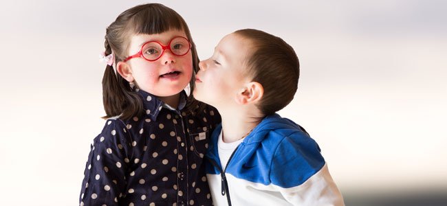 Niña con síndrome de Down recibiendo un beso en la mejilla de otro niño más pequeño.