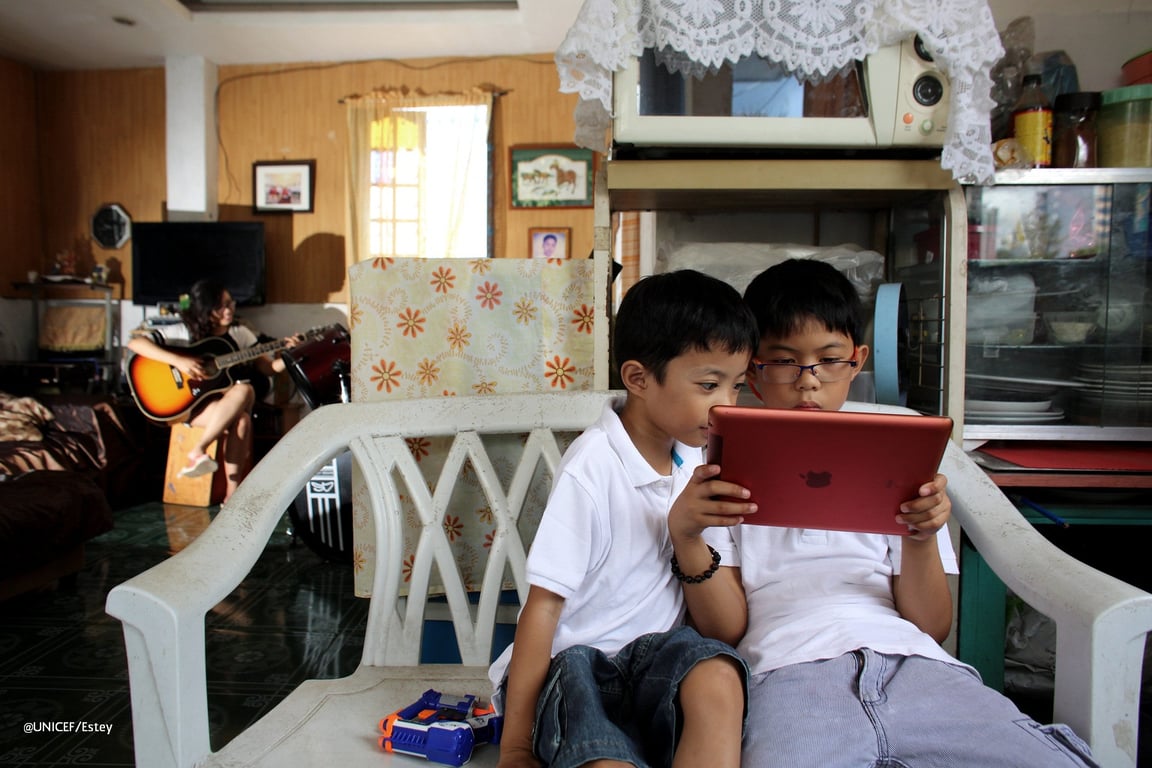 Dos niños latinos sentados en el sofá viendo una tablet.