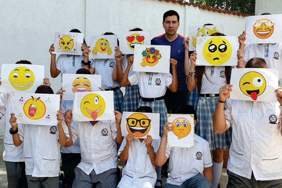 Alumnos con emoticones impresos frente a su rostro y el profesor Eduardo Esteban Pérez al centro sonriendo.