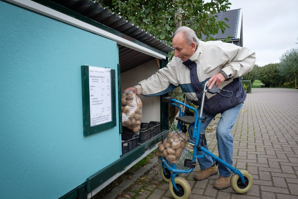 Adulto mayor llevando bolsas de papas a un depósito en una andadera especial con canasta.