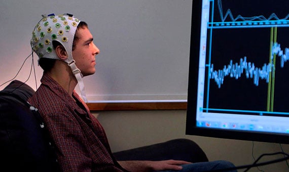 Persona con conexiones de cables sobre su cabeza viendo un monitor de frente.