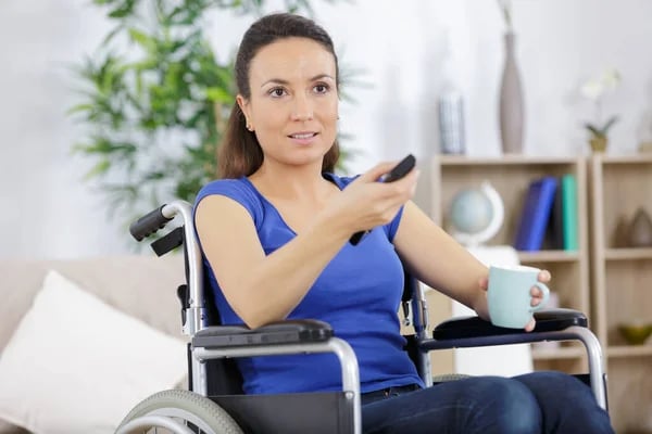 Mujer con discapacidad motriz usuaria de silla de ruedas con un control remoto en su mano.