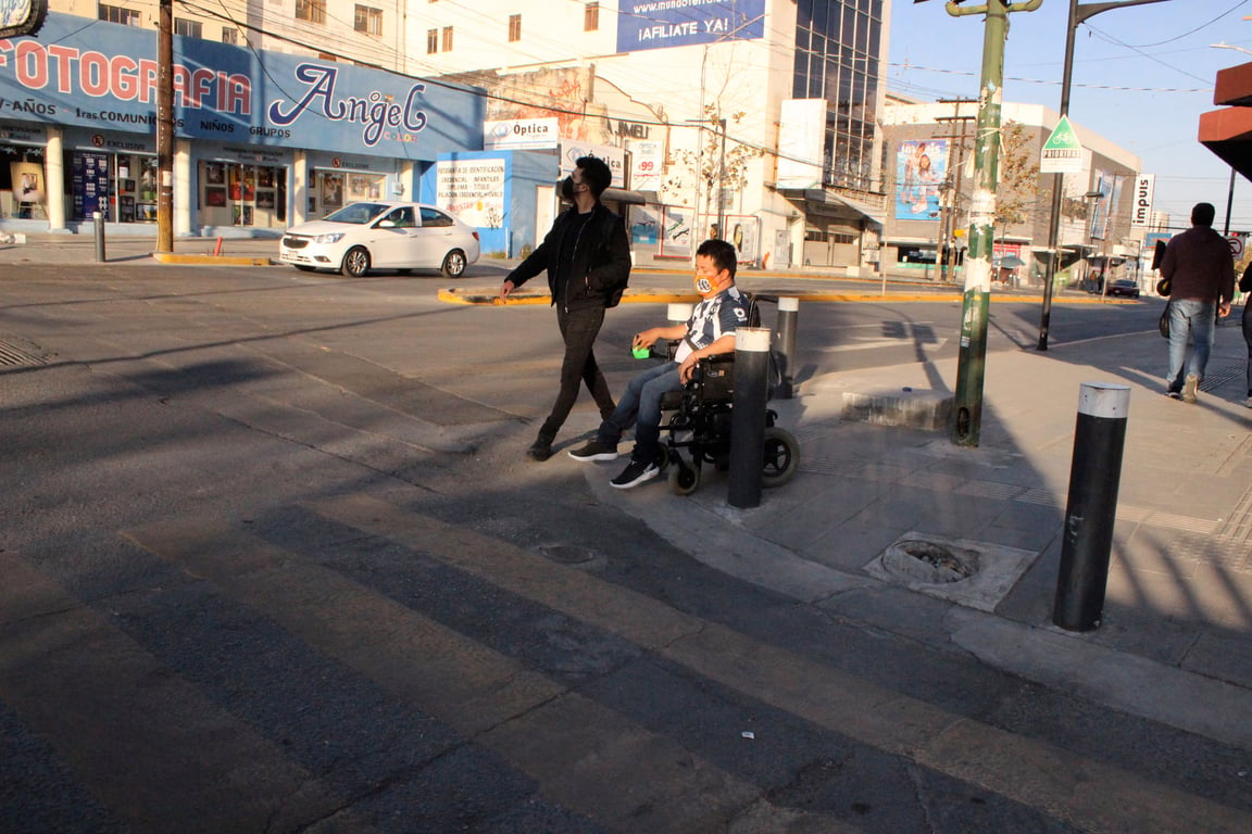 Usuario de silla de ruedas cruzando con dificultad una avenida sin rampa.