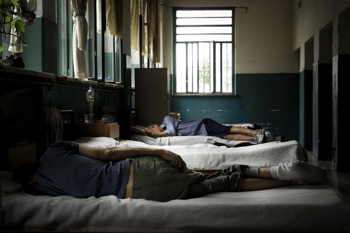 Dos hombres recostados en camas de un hospital psiquiátrico.