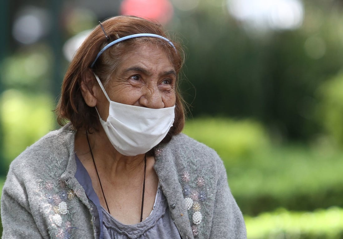 Adulta mayor sentada en un parque con un cubrebocas debajo de la nariz.