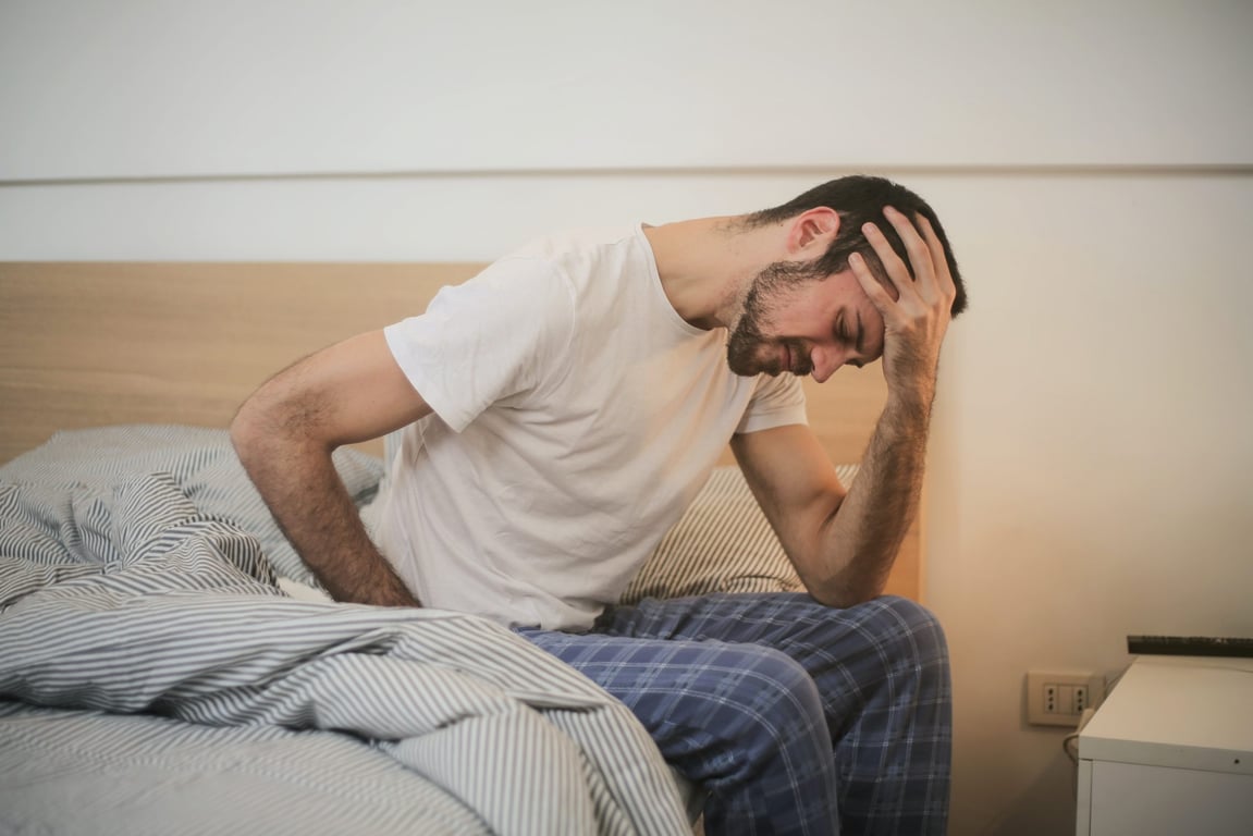 Hombre recostado en su cama con dolor de cabeza.