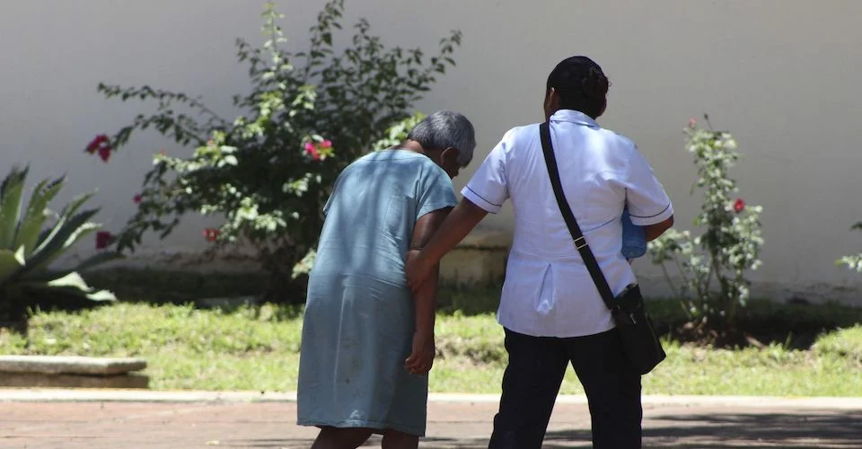 Enfermero llevando del brazo a una anciana cabizbaja.