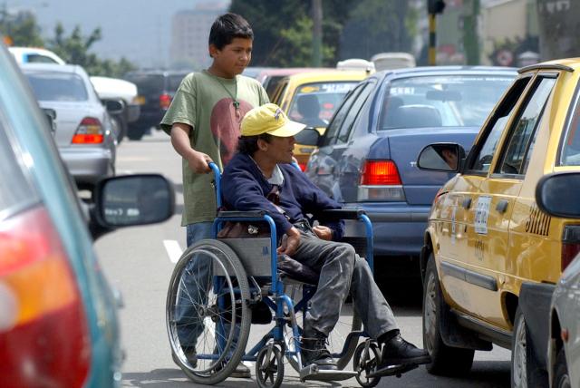 Usuario silla de ruedas pidiendo dinero a automóviles durante un semáforo en alto.