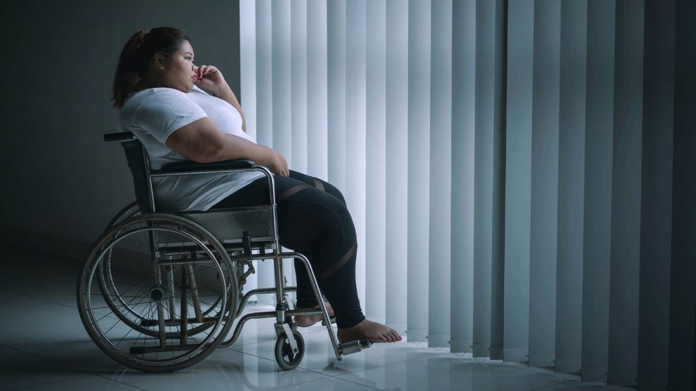 Usuaria de silla de ruedas con obesidad frente a una ventana.