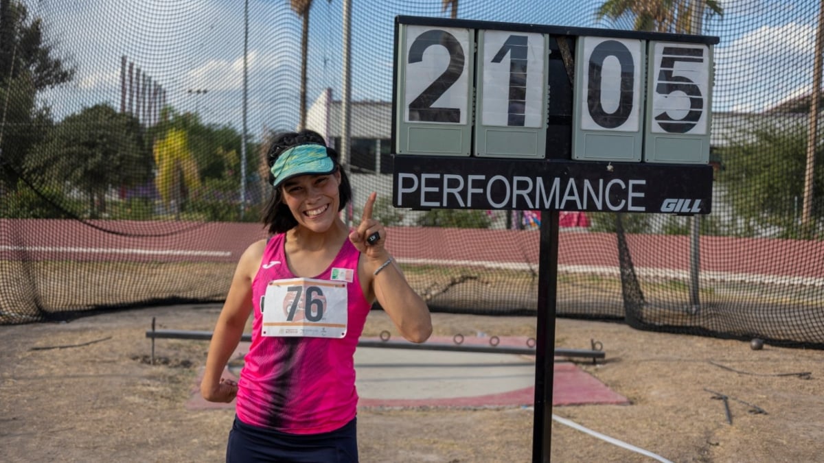 Fotografía de una atleta con parálisis cerebral junto a la pancarta que registra su lanzamiento de 21.05 metros para imponer el récord en América
