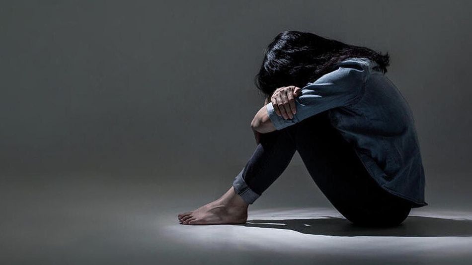 Mujer deprimida abrazando sus piernas dentro de un cuarto oscuro.