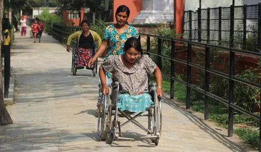 Usuaria de silla de ruedas viste con un huipil y es guiada por otra mujer con huipil.