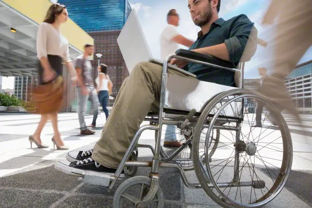 Usuario de silla de ruedas en medio de la calle transitada por varias personas.