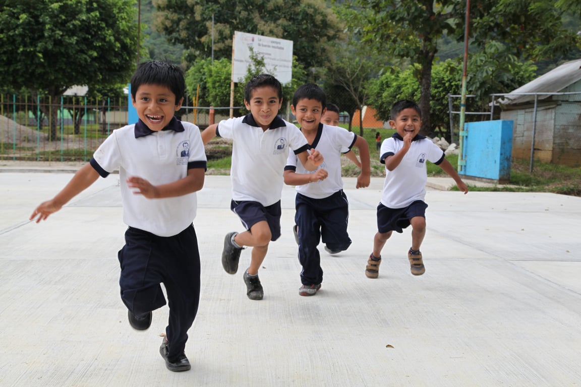 Niños uniformados corriendo en el patio de una escuela.