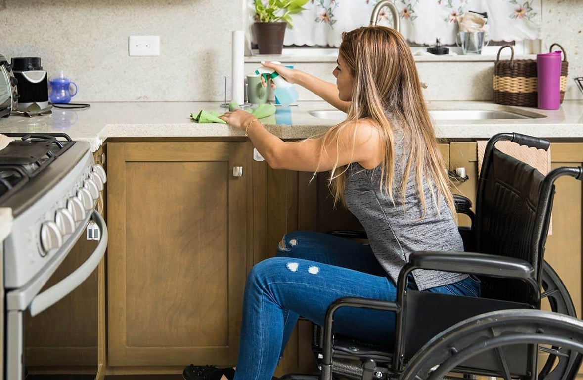 Usuaria en silla de ruedas lavando trastes en una cocina adaptada para personas con discapacidad.