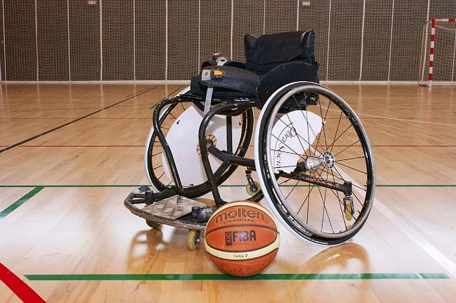 Silla de ruedas al centro de una duela de básquetbol con un balón de baloncesto al frente.